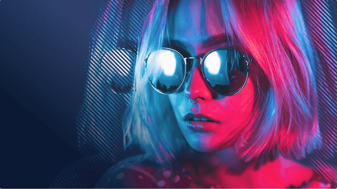 A girl wearing aviator sunglasses with a neon pink and blue glow on her face.